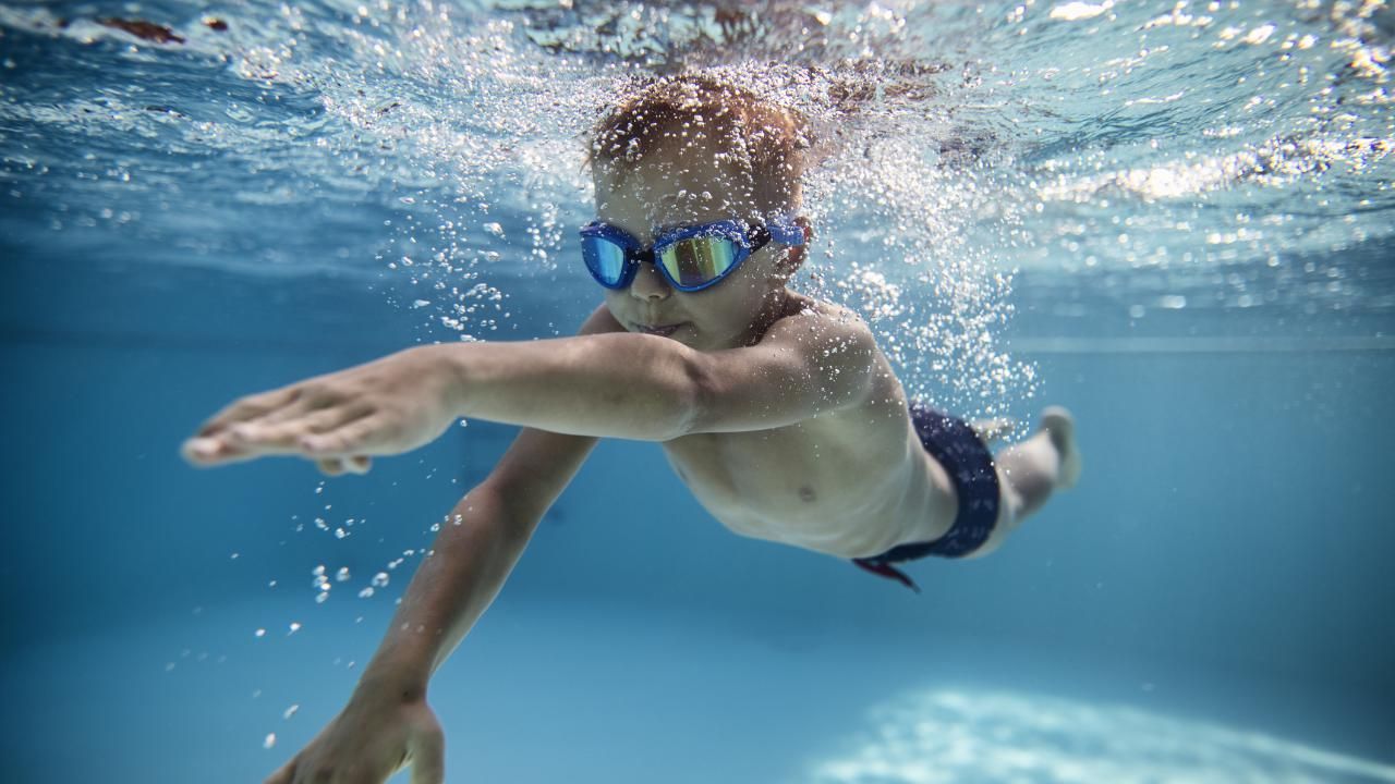 Bambino che nuota sott'acqua con occhialini